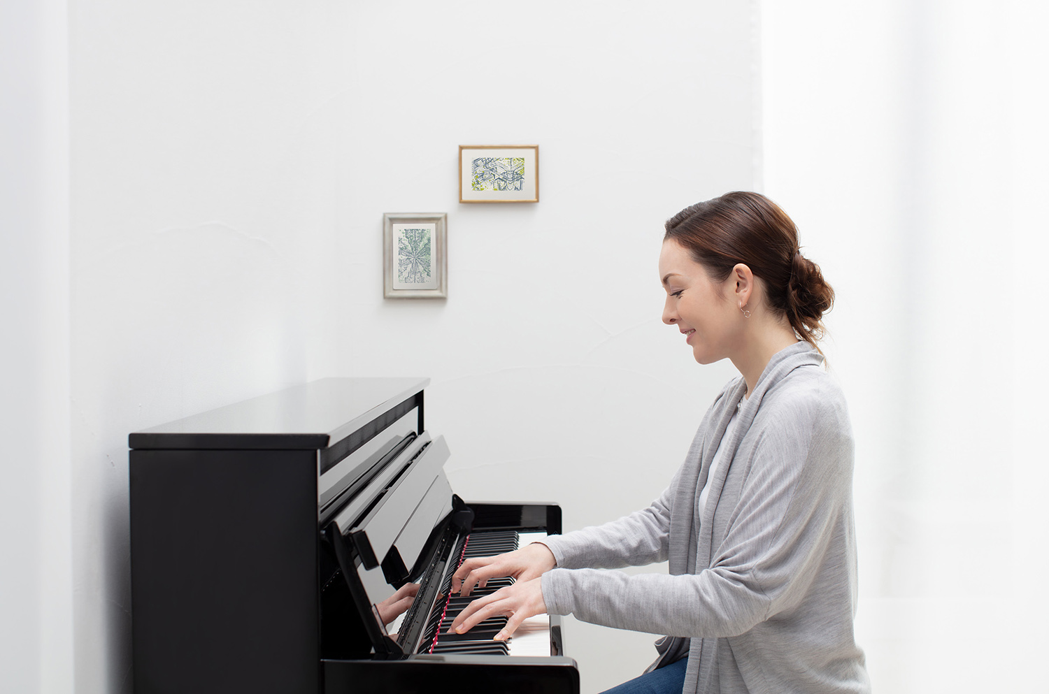 Woman playing Kawai K-15 upright piano in modern style room, demonstrating exceptional tone and touch.