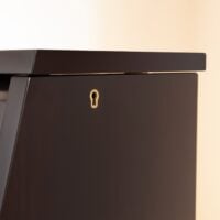 Glossy ebony upright piano cabinet corner detail with keyhole lock, showcasing premium craftsmanship and elegant design.
