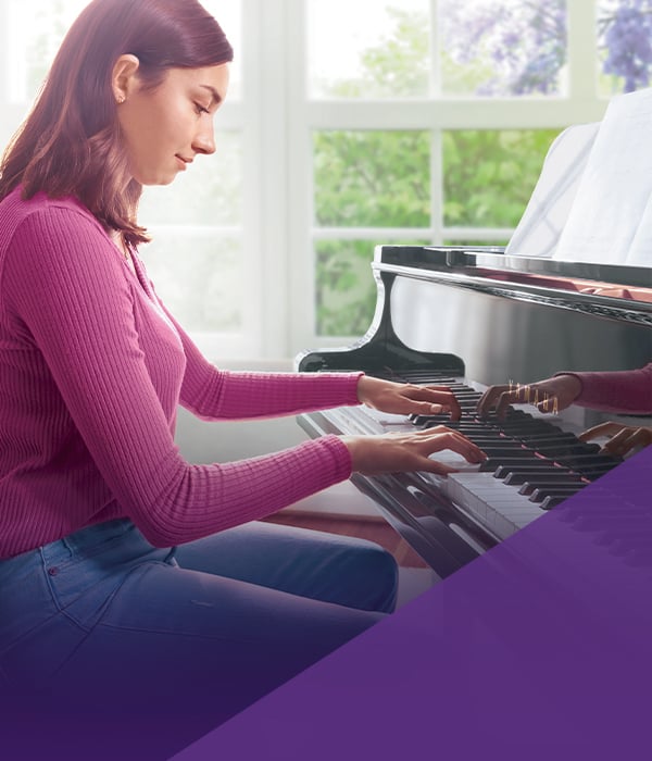 Young woman playing a polished ebony grand piano, showcasing its rich sound and elegant craftsmanship at Classic Pianos.