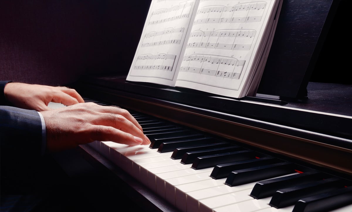 Close-up of hands playing a grand piano, with sheet music displaying classical compositions, showcasing premium craftsmanship.