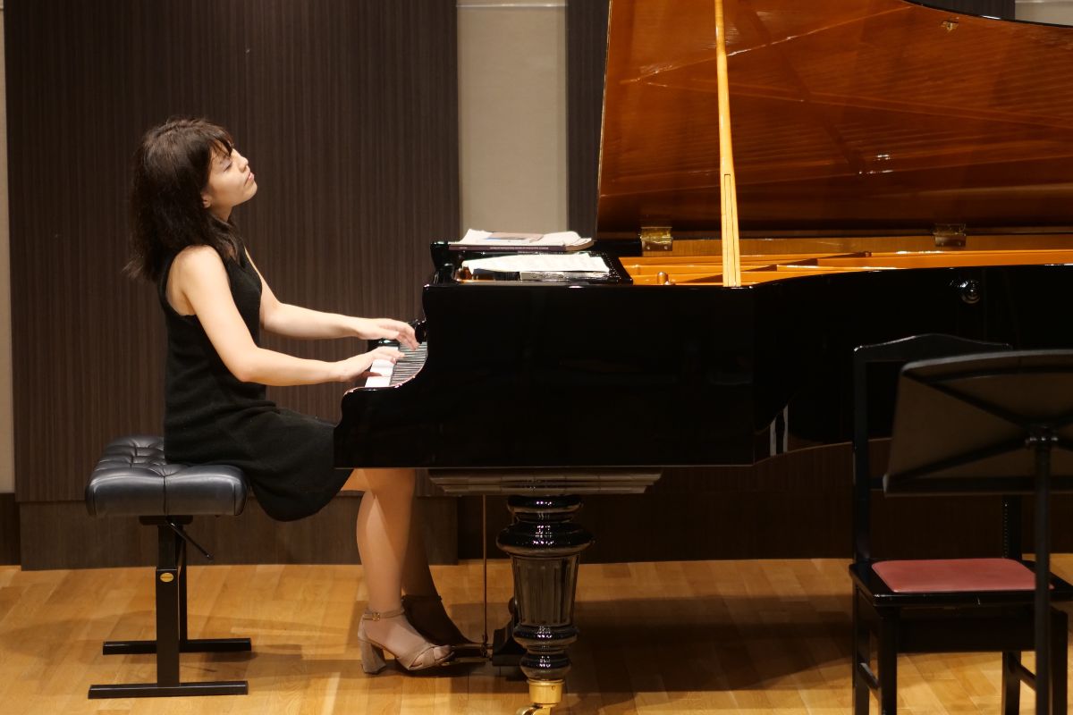 Children gathered around a piano, engaging in a fun learning session under expert guidance. Promoting musical skills. Young woman playing used but well-maintained institutional piano.
