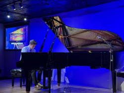 Performer playing a Steinway grand piano in a modern showroom, showcasing rich mahogany finish and premium sound quality.